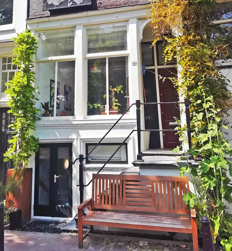 Exterior of Sally’s Fault artist space in Amsterdam with vines, narrow doorway and wooden bench.